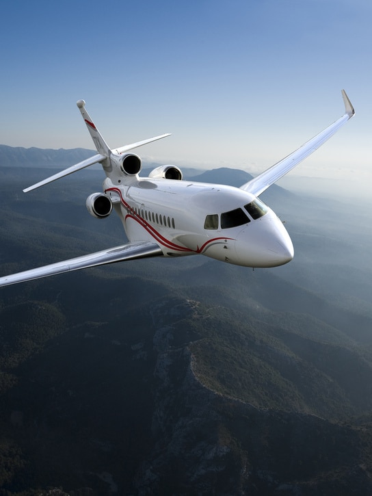 Dassault Avion Falcon 7X survolant une chaîne de montagnes, illustrant l’élégance et la qualité associées à un site vitrine luxe créé pour valoriser des aménagements intérieurs premium.